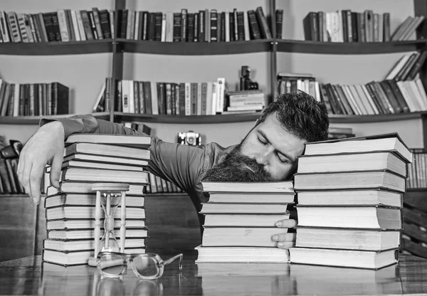 Concepto sobreestudiado. Profesor o estudiante con barba duerme en libros, desenfocado. Hombre en la cara dormida yacía entre montones de libros, dormirse mientras estudiaba en la biblioteca, estanterías en el fondo —  Fotos de Stock