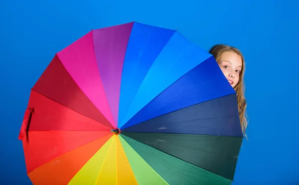 Weather forecast concept. Stay positive though rainy day. Brighten up life. Kid peek out colorful rainbow umbrella. Color your life. Girl cheerful hide behind umbrella. Colorful umbrella accessory
