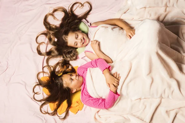 Kids in pink pajamas under white blanket. Children with smiles — Stock Photo, Image