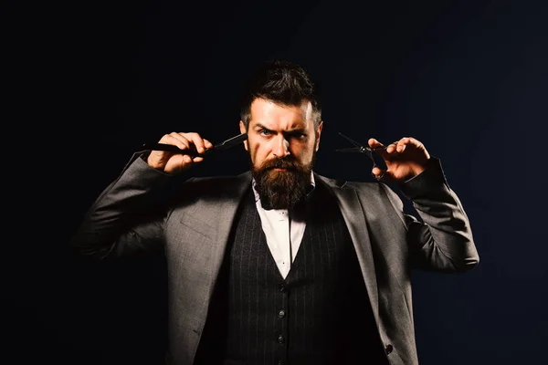 Man with long beard holds shaving razor and scissors.