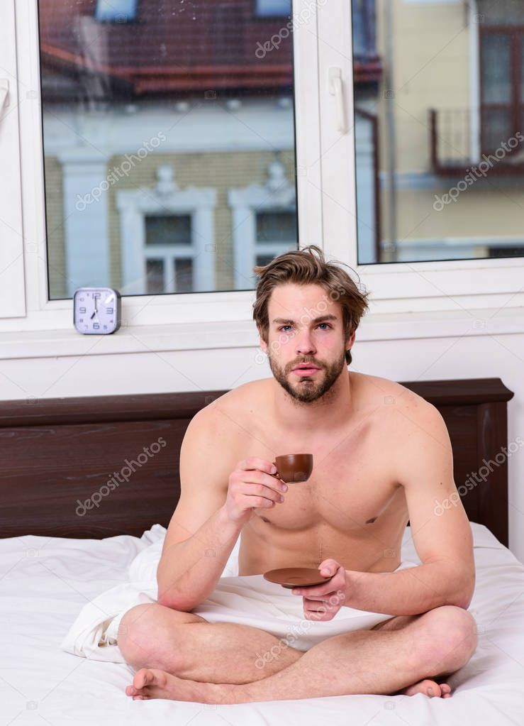 Man handsome macho with muscular torso relaxing on bed with cup of coffee. Coffee fills you with energy. Every morning with his coffee. Begin good day. How coffee affects your body from first sip