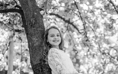 Sakura, ağaç gövdesinde yalın yakın duran yüz gülümseyerek kıza. Açık uzun saçlı kız, kiraz çiçeği veya sakura arka plan üzerinde. Şirin çocuk Doğa bahar sabahı keyfini çıkarın. Doğa kavramı ile birleştirmek
