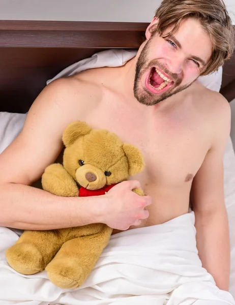 Guy hug teddy bear soft plush toy. Man unshaven bearded face relax with favorite teddy bear. Sweet dreams concept. Man handsome guy relaxing bed hug teddy bear toy. Sweet memories from childhood