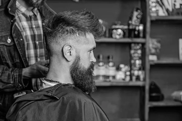 Hairstyle service concept. Hipster bearded client got hairstyle. Barber with clipper works on hairstyle for bearded man, barbershop background. Barber with trimmer or clipper shaved neck of client