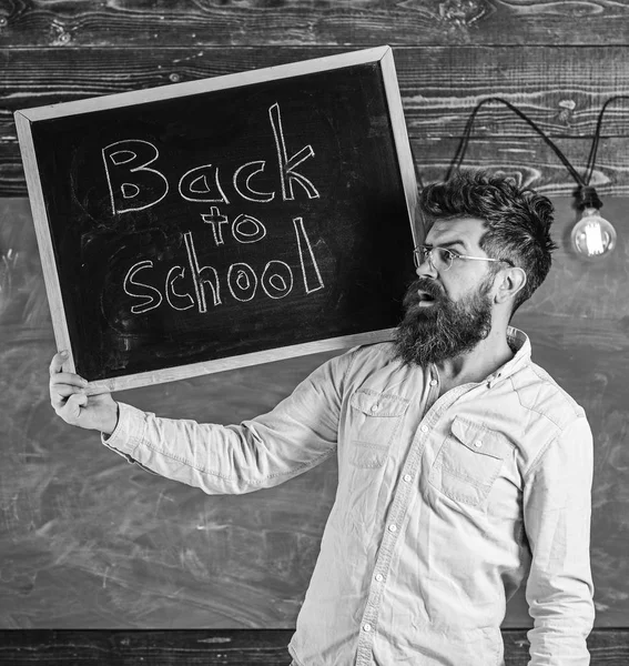 High school concept. Man with beard and mustache on surprised face welcomes students, chalkboard on background. Teacher in eyeglasses holds blackboard with title back to school — Stock Photo, Image