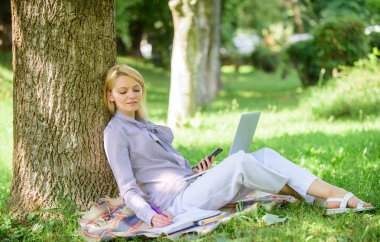 Dizüstü bilgisayar işleriyle açık havada ağaç gövdesinde yağsız olan kadın. Park içinde laptop ile kız iş çimenlerin üzerinde oturmak. Doğal çevre ofisi. Açık havada faydaları iş. Eğitim teknolojisi ve internet kavramı