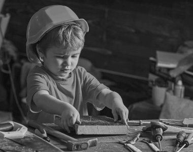 Kask oluşturucu veya repairer, onarımı veya handcrafting olarak oynayan sevimli çocuk. Meşgul yüz oyunlarında evde atölye üzerinde yürümeye başlayan çocuk. Kavram handcrafting. Çocuk çocuk dövülmüş tırnak içine ahşap tahta