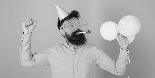 Homem barbudo em boné de aniversário e enormes óculos loucos dançando, festa difícil, conceito de tempo divertido. Hipster com barba aparada e bigode posando com apito de festa e balões brilhantes no fundo azul — Fotografia de Stock