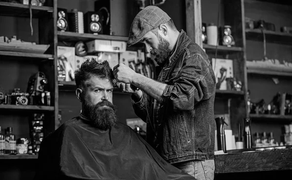 Un client hippie qui se fait couper les cheveux. Barbier avec tondeuse à cheveux travaille sur la coiffure pour barbe homme fond de salon de coiffure. Concept de mode de vie hippie. Barbier avec tondeuse couper les cheveux sur le temple du client — Photo