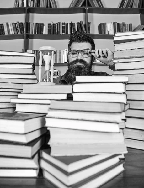 Concepto de flujo de tiempo. Profesor o estudiante con barba estudiando en la biblioteca. El hombre con cara seria viendo el tiempo está pasando, estanterías en el fondo. Hombre, científico en gafas mira hourglas — Foto de Stock