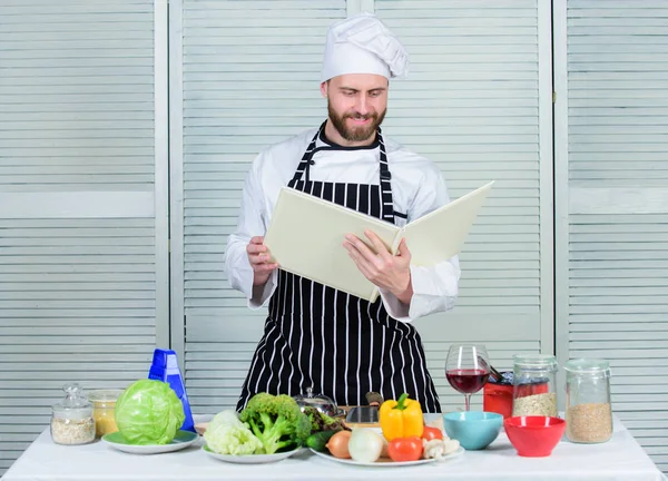 Guy read book recipes. Culinary arts concept. Man learn recipe. Improve cooking skill. Book family recipes. Ultimate cooking guide for beginners. According to recipe. Man bearded chef cooking food — Stock Photo, Image