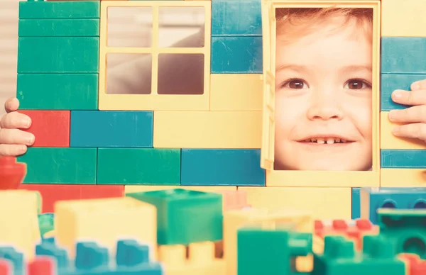 Niño juega con ladrillos de construcción, mirando a través de la puerta de juguete — Foto de Stock