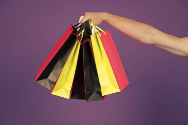 Menekşe arka plan üzerinde elinde poşetler. Farklı renklerde kağıt torbalar. Çanta veya paperbags. Alışveriş veya satış ve siyah Cuma kavramı. Tatil hazırlanması ve kutlama. Hediye ve hediye