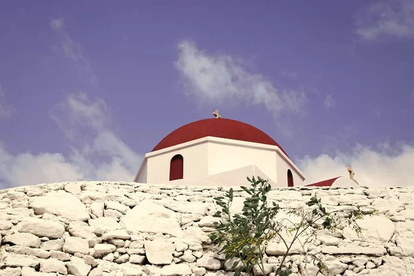 Recinzione in pietra e cupola rossa con dettaglio a croce a Mykonos, Grecia. Chiesa edificio architettura su soleggiato all'aperto. Cappella sul cielo blu. Religione e concetto di culto. Vacanze estive sull'isola mediterranea — Foto Stock