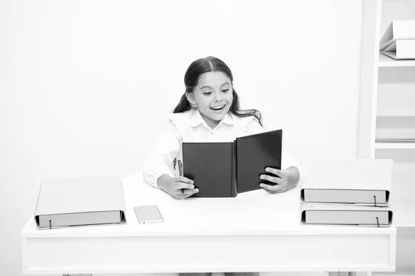 Takové zajímavé téma. Dívka dítě číst knihu zatímco sit stůl bílý interiér. Učebnice čtení. Školačka studium učebnice. Kluk holka školy jednotná šťastný obličej číst knihu. Nadšený správnou odpověď — Stock fotografie