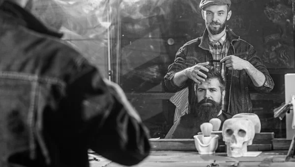 Hombre con barba y bigote en silla de peluquería frente al fondo del espejo. Reflexión de peluquero peinado pelo de cliente barbudo con peine. Hipster cliente conseguir peinado. Concepto de barbería —  Fotos de Stock