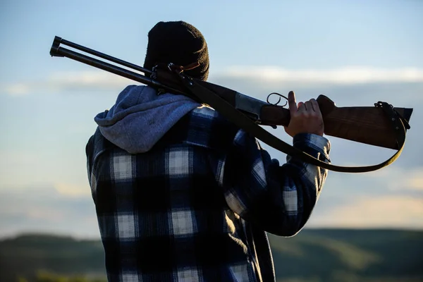 Hunting masculine hobby leisure concept. Brutality and masculinity. Hunter carry rifle gun on shoulder rear view. Guy hunter spend leisure hunting. Man brutal guy gamekeeper in hat nature background — Stock Photo, Image