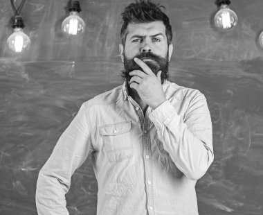 Sakal ve bıyık düşünceli yüz stand önünde kara tahta üzerinde olan adam. Fikri görev kavramı. Adam düşünceli ifade ile düşünme. Gömlek, arka plan kara tahta sakallı hippi