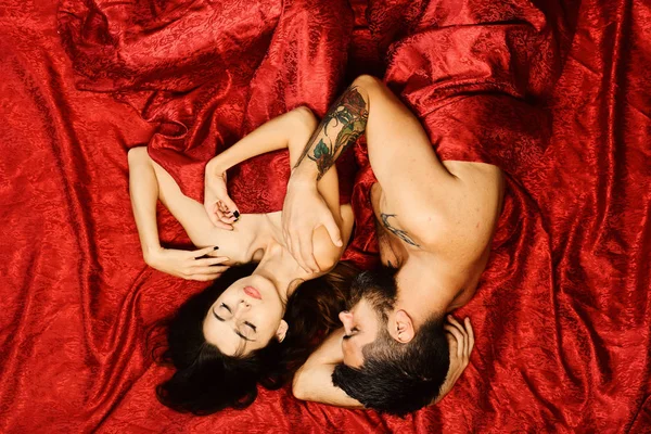 Birbirine aşık çiftler kırmızı çarşaflarda yatar. Erkek ve kadın. — Stok fotoğraf