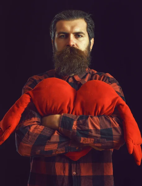 Bonito barbudo homem ou cara em xadrez camisa com bigode na moda e barba no rosto sério detém valentines vermelho coração travesseiro no preto backgroun — Fotografia de Stock