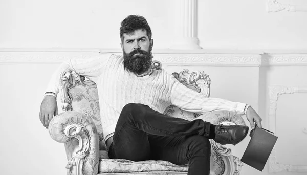 Hombre con barba y bigote se sienta en el sillón, sostiene libro, fondo blanco de la pared. Conocedor de cara reflexiva terminado libro de lectura. Un tipo pensando en literatura. Conocedor del concepto de literatura — Foto de Stock