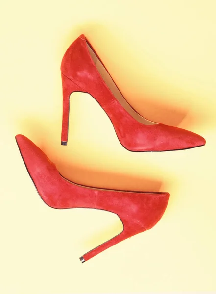 Luxury footwear concept. Footwear with thin high heels, stiletto shoes, top view. Shoes made out of red suede on yellow background. Pair of fashionable high heeled pump shoes