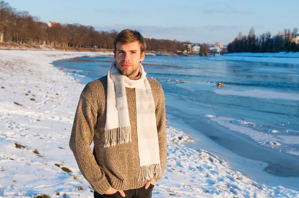 Hombre sin afeitar guapo hipster en punto suéter bufanda de lana soporte congelado río fondo. Paisaje de invierno belleza. El hombre disfruta del día soleado de invierno. Moda de invierno. Ropa de punto de invierno calentando —  Fotos de Stock