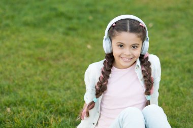 Çocuk kız yeşil çim çayır oturup müzik keyfini çıkarın. Hoş serbest zaman. Çocuk kulaklık müzik dinle. Çok güzel kız moda müzik dinlerken kulaklık. Açık dinlenirken müzik dinle