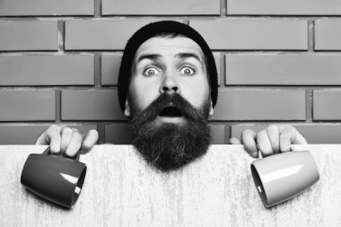 Sakallı adam, uzun sakallı. Kahverengi tuğla duvar arka planında elinde renkli fincanlar tutan, siyah şapkalı, traşsız, beyaz bir hippi.