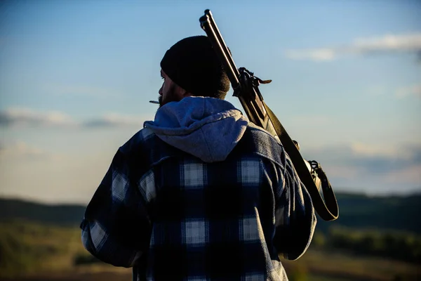 Guy Hunter pasa tiempo libre cazando. Caza masculina hobby concepto de ocio. Hombre tipo brutal guardabosques en el fondo de la naturaleza sombrero. Brutalidad y masculinidad. Hunter llevar pistola de rifle en el hombro vista trasera — Foto de Stock