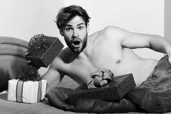 Mladý pohledný vousatých sexy macho muž s stylový plnovous ležel nahý na posteli pod červenou deku s dárky nebo Valentýnské dárky na barevné poza — Stock fotografie