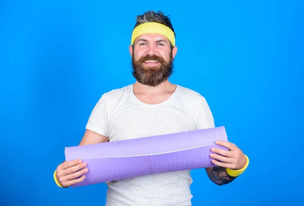 Man bearded athlete hold fitness mat blue background. Lets start yoga class. Yoga as hobby and sport. Practicing yoga every day. Stay in shape. Athlete professional yoga coach motivated for training