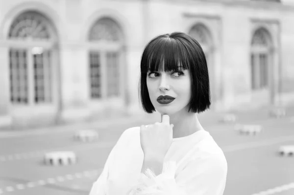 Una mujer misteriosa tiene una idea. Chica de moda dama con peinado bob al aire libre de la arquitectura urbana de fondo. Mujer modelo de moda posando al aire libre. Chica morena bob peinado se ve elegante — Foto de Stock