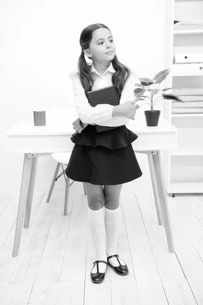 Excellent first former. Girl child hold book while stand table white interior. Kid school uniform happy face hold book. Confident about knowledge. Ready enter first form. Schoolgirl studying textbook — Stock Photo, Image