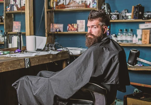 Człowieka z brodą, pokryte czarną, cienką pelerynę siedzi w fotelu Fryzjer przed lustrem. Człowiek z broda klienta hipster fryzjera. Koncepcja fryzjera. Hipster z brodą czeka na fryzjera i fryzura — Zdjęcie stockowe