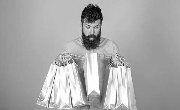 Πώληση και έκπτωση έννοια. Hipster σε σοκαρισμένη πρόσωπο ψώνια εθισμένος ή shopaholic. Ο άντρας με γενειάδα και μουστάκι κουβαλάει τσάντες για ψώνια, γαλάζιο φόντο. Guy ψώνια για την περίοδο πωλήσεων με εκπτώσεις — Φωτογραφία Αρχείου