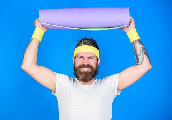 Stay in shape. Athlete professional yoga coach motivated for training. Man bearded athlete hold fitness mat blue background. Lets start yoga class. Yoga as hobby and sport. Practicing yoga every day