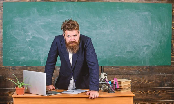 Profesor estricto hombre barbudo serio se inclinan sobre el fondo de pizarra de mesa. El profesor parece amenazador. Reglas de comportamiento escolar. Hombre infeliz con el comportamiento. Director de escuela amenazando con castigo —  Fotos de Stock