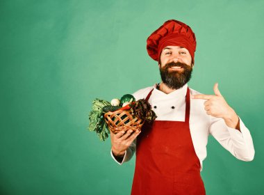 Mutlu yüzlü, bordo üniformalı aşçı sebzeleri işaret ediyor.