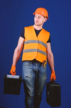 Kask, kask içinde adam araç kutusu ve araç, mavi arka plan ile bavul tutar. Tamirci, tamirci konsantre yüzündeki profesyonel ekipman ile ağır çanta taşır. Profesyonel tamirci kavramı