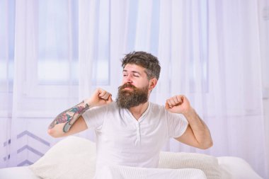 Adam silah, sabah enerji dolu germe. Mükemmel sabah kavramı. Nap sonra rahatlatıcı maço memnun yüz germe üzerinde bekletin. Tişörtlü adam yatak, beyaz perde arka plan üzerinde oturur