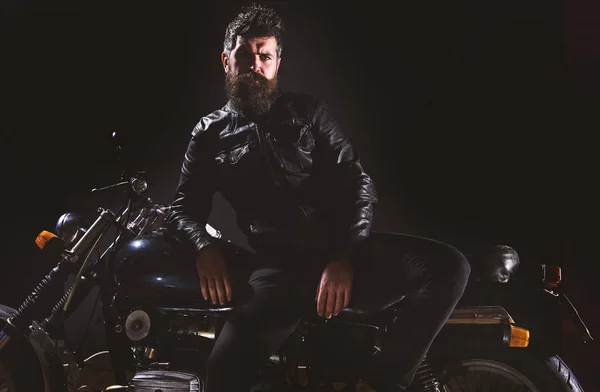 Macho, motard brutal en veste en cuir se tenir près de la moto la nuit, l'espace de copie. Concept de culture motard. Homme à la barbe, motard veste en cuir maigre sur moto dans l'obscurité, fond noir — Photo