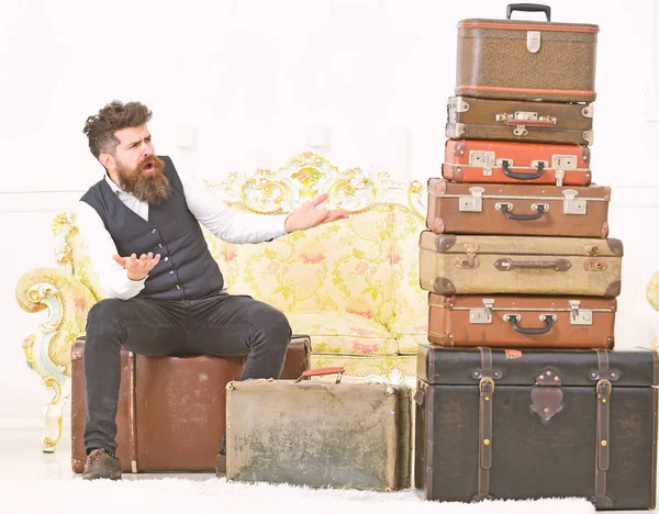 Macho elegant auf überraschtem Gesicht sitzt schockiert neben einem Stapel Vintage-Koffer. Gepäck und Reisekonzept. Mann, Butler mit Bart und Schnurrbart liefert Gepäck, luxuriöser weißer Innenraum — Stockfoto