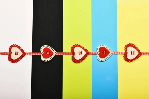 Handmade decoration on colourful striped background. Checked ribbon with red and white hearts beaded on it. Valentines day and love concept. Holiday card