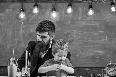 Çocuk ve öğretmen meşgul yüzleri boyuyor, resim çiziyor. Sakallı öğretmen, baba ve küçük oğlu sınıfta resim çizerken, yaratırken, arka planda karatahta çizerken. Yetenek ve yaratıcılık kavramı