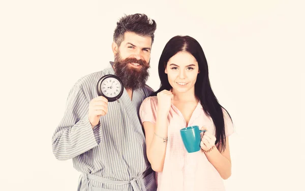 Man and girl in pajamas get up on time, white background. Perfect morning with coffee. Couple in love drink morning coffee or tea. Family of man and woman with cup and alarm clock