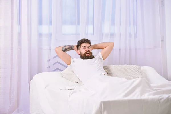 穿衬衣的男人躺在床上, 背景上是白色的窗帘。人在满意的脸上充满活力的早晨。充满力量和能量的概念。有胡子的男人拿着手在头后, 放松 — 图库照片