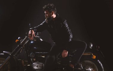 Sakallı, bisikletçinin yalın motorlu bisiklet karanlıkta siyah arka plan üzerinde deri ceketli adam. Motorcu kültür kavramı. Maço, vahşi Motorcu deri ceketli stand motosiklet gece zaman, kopya alanı