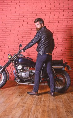 Erkeksi hobi kavramı. Yenilikçi, vahşi Motorcu deri ceket ciddi yüzüne üzerinde motosiklet üzerinde oturur. Sakallı, motorcu motorlu bisiklet garaj, tuğla duvar arka plan yakınındaki deri ceketli adam