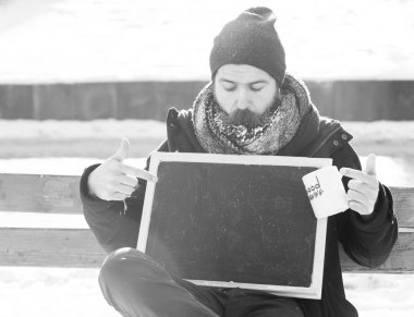 Yakışıklı adam, beyaz frost, boş kara tahta noktalarda hipster sakal ve bıyık ile kaplı veya kara tahta holding ile Günaydın metin doğal zemin üzerine kış gününde Kupası, girintili Kopyala